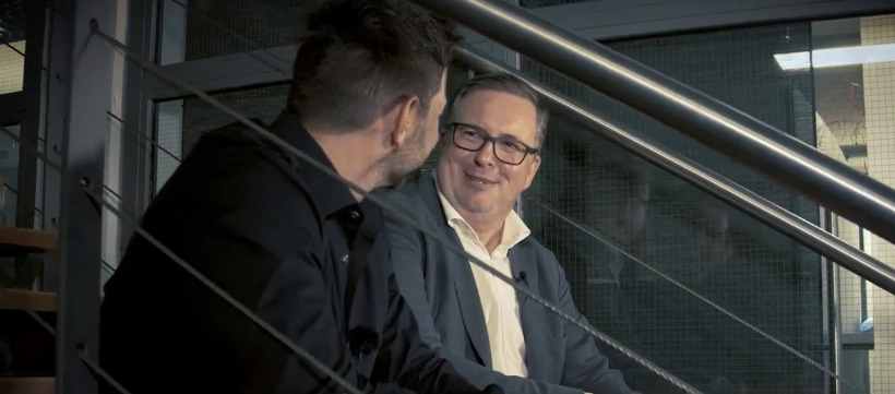 Auf Bild ist Martin Berchtenbreiter mit Sven Zuschlag auf einer Treppe und sie unterhalten sich sitzend